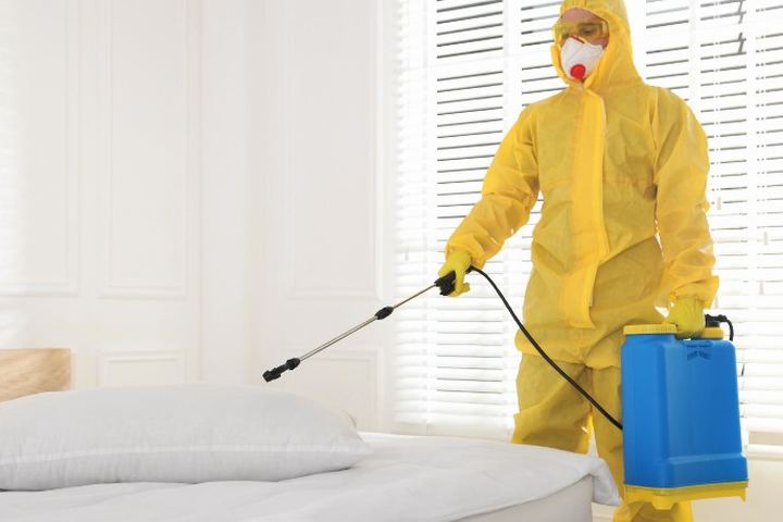 Aplicador con buzo amarillo y mascarilla trata con lanza el somier y el perímetro del colchón de un dormitorio