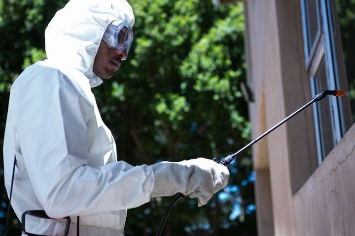 Aplicador con buzo blanco y gafas de protección trata con lanza el encuentro entre la fachada y la ventana de una vivienda