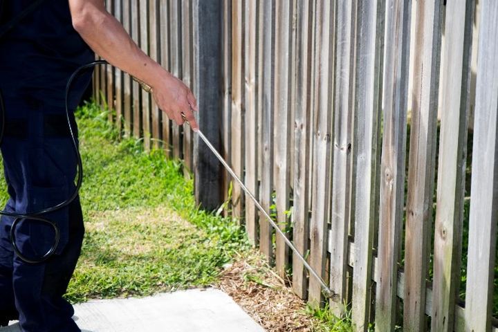 Técnico aplica con lanza larga una banda de producto en la base del cerramiento de madera de una parcela ajardinada