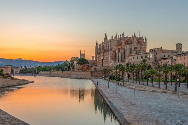 Catedral de Palma reflejada en el lago del Parc de la Mar al atardecer, con el paseo de palmeras en primer plano
